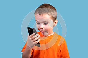 A little boy looks at the phone, and is surprised. Isolated on a blue background