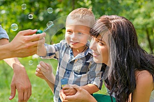 A little boy looks on a soap bubbles. Dad holds his son`s hand a