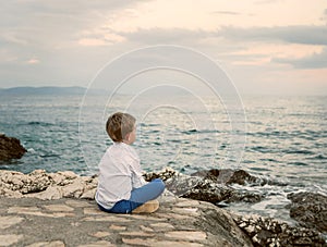 Little boy looks on the sunset sea landscape