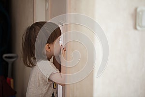 The little boy looks in the window of the door. A child spying on his parents from behind the closed bedroom door