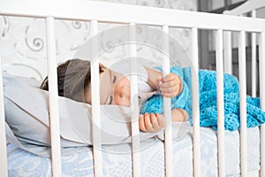 Little boy lying alone in crib. Sad little baby. Waif child. Loneliness.