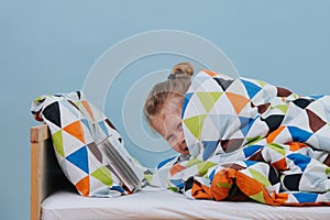Little boy lying in bed, pretending to read until his parents leave