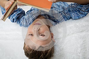 Little boy is lying on the bed and reading a book