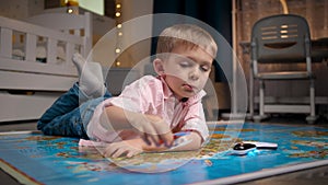 Little boy lying on big map and pretending to fly around the world on toy airplane. Concept of travel, tourism and child