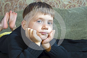 Little boy is lying on the couch and is looking at the camera