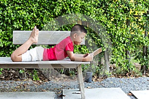 Little boy lying on the wooden bench reading a book
