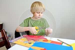 Little boy making colored paper crafts at home. Child cuts scissors details. Creativities lessons, distance learning,