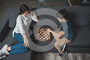 Little boy making a move in chess while playing with his mom on couch