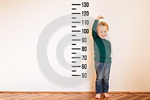 Little boy measuring height near white wall. Copy space