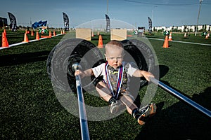 Little boy with a medal around his neck between two heavy barbells