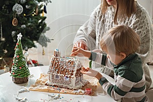 Little boy with mother decorating christmas gingerbread house together, family activities and traditions on