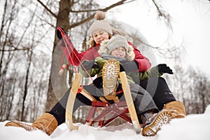 Little boy and mother enjoy sliding on the snow slide