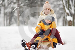 Little boy and mother/grandmother/nanny sliding in the Park during a snowfall