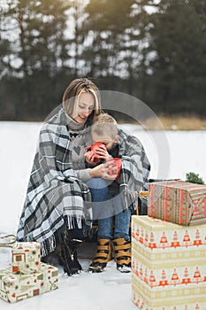 Little boy and mother sliding in the winter forest. Mom and son sitting on the sledge, covering by the checkered plaid