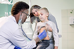 Little boy with mother visiting children`s African American doctor with stethoscope in hospital