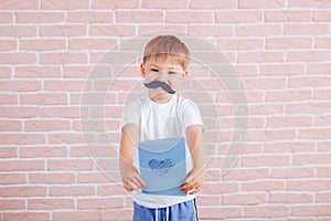 Little boy with a mustache holding a gift in his hands, father`s day, mother`s day