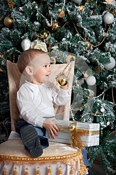 Little boy near fir tree with Christmas gift. Indoor