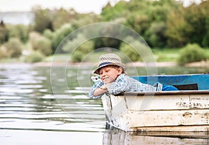Little boy in old boat on the calm lake surface