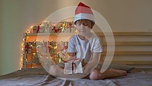 A little boy opening a present from an advent calendar which is hanging on a bed that is lightened with christmas lights