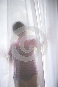 Little boy opening standing behind the white curtain