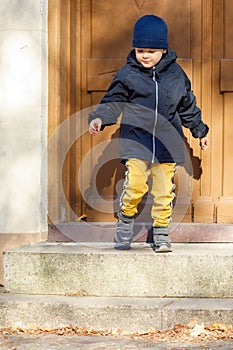 The little boy opens the big brown entrance door. The child leaves the house for an autumn walk