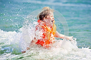 Little boy in orange life vest swimming in wave sea