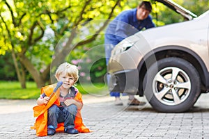 Little boy in orange safety vest during his father repairing family car
