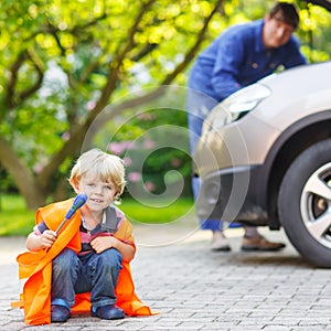 Little boy in orange safety vest during his father repairing family car