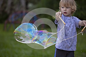 Young, 4 year old preschool boy with a grey shirt and blond hair, blowing bubbles in the yard