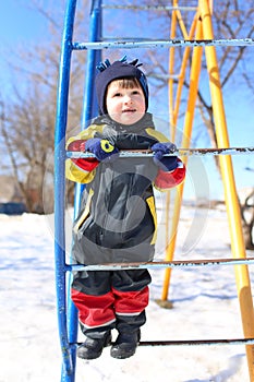 Little boy in overall plays on climber in winter