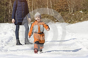 Little boy in overalls runs away from his mother. Winter snowy day in the coniferous forest