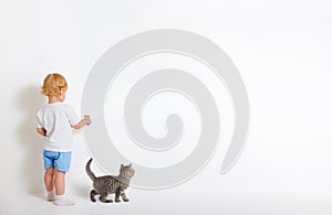 Little boy with paint brush and small cat standing back near white wall