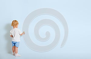 Little boy with paint brush standing back near blue wall