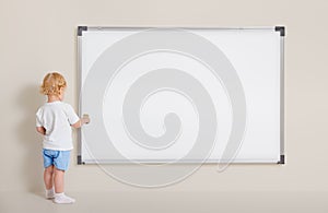 Little boy with paint brush standing near blank whiteboard