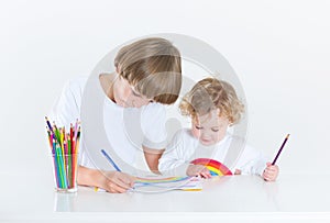 Little boy painting at white desk with toddler sister