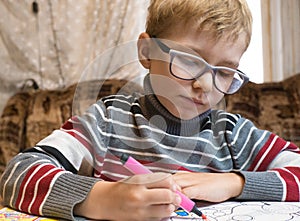 A little boy paints a coloring with crayons and felt-tip pens on a wooden table at home