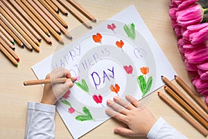 Little boy paints greeting card for Mom on Mother`s Day with the inscription `Happy mother`s day`.