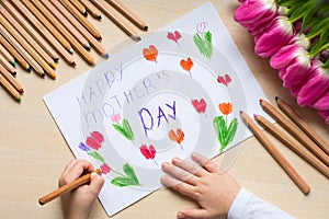 Little boy paints greeting card for Mom on Mother`s Day with the inscription `Happy mother`s day`.