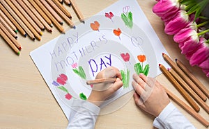 Little boy paints greeting card for Mom on Mother`s Day with the inscription `Happy mother`s day`