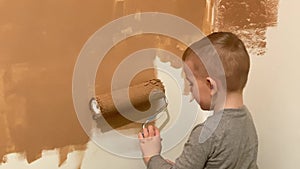 A little boy paints a wall in his room in terracotta with a roller