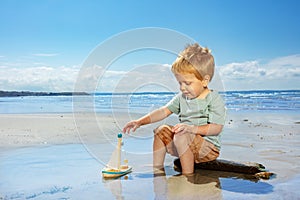 Little boy paly with toy sail ship on the beach