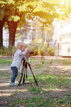 Little boy photographing on the camera on tripod in the park