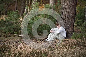 Little boy in a pinewood forest sitting among pine cones