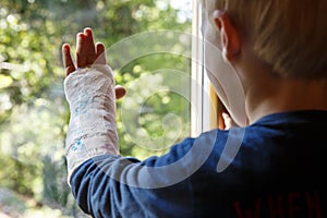 Little boy with a plaster on his arm looking through the window