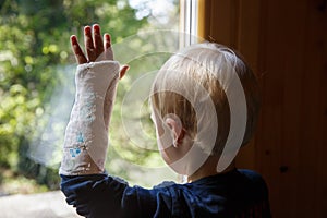 Little boy with a plaster on his arm looking through the window