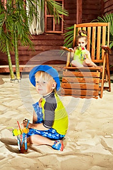 Little boy play in sand, his sister sits in wooden