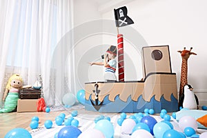 Little boy playing with binoculars in pirate cardboard ship at home. Child`s room interior