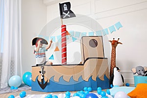 Little boy playing with binoculars in pirate cardboard ship at home. Child`s room interior