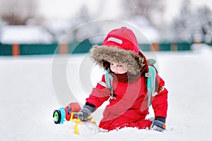 Little boy playing with bright car toy and fresh snow