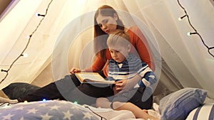 Little boy playing in children`s tent at home. Mother reading fairy tale book. Happy caucasian kid in the playroom.